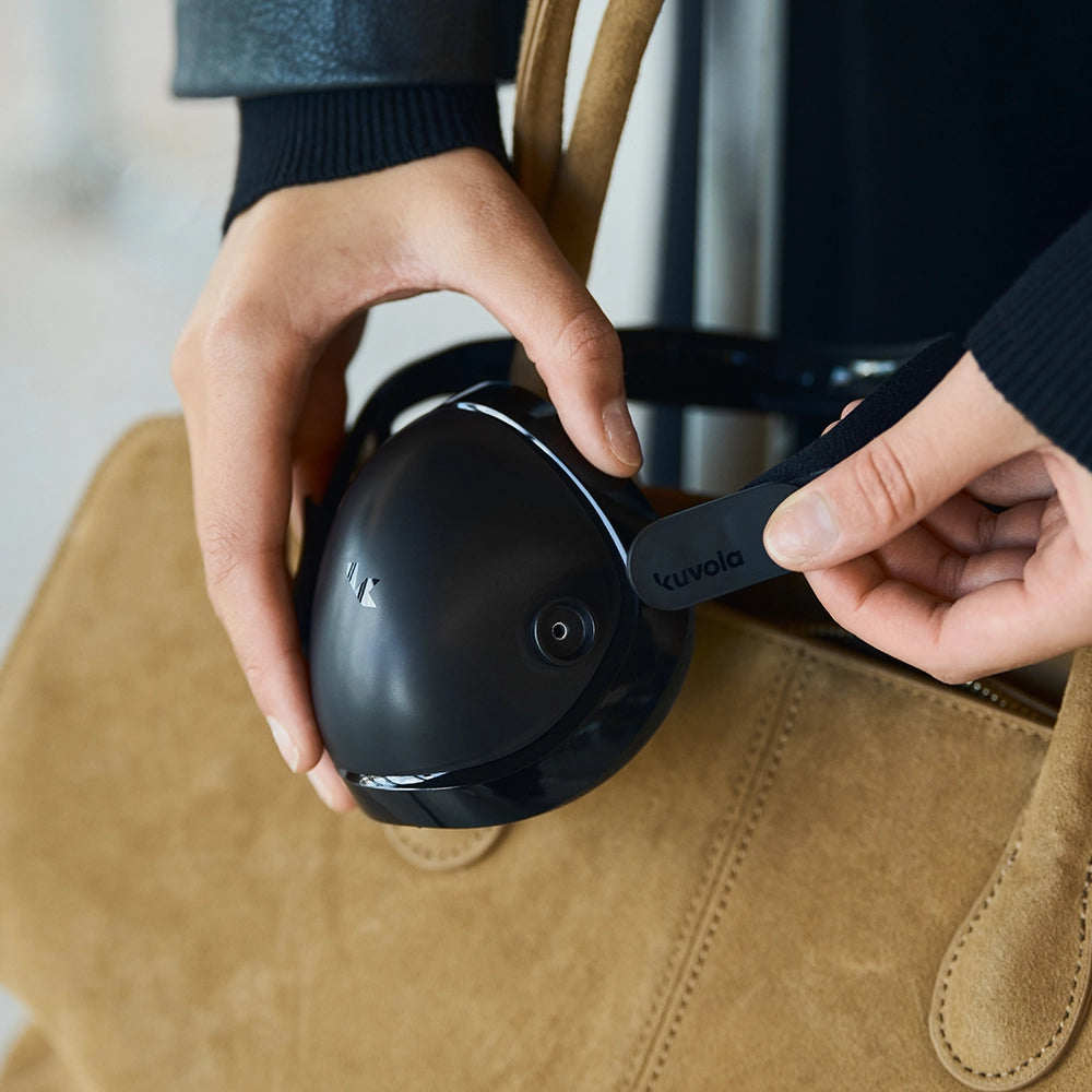 Person holding a black device with 'kuvola' branding against a brown bag.