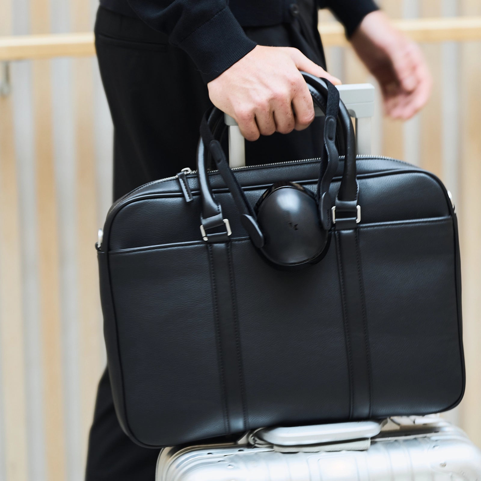 Person holding a black leather briefcase on a suitcase in an airport.