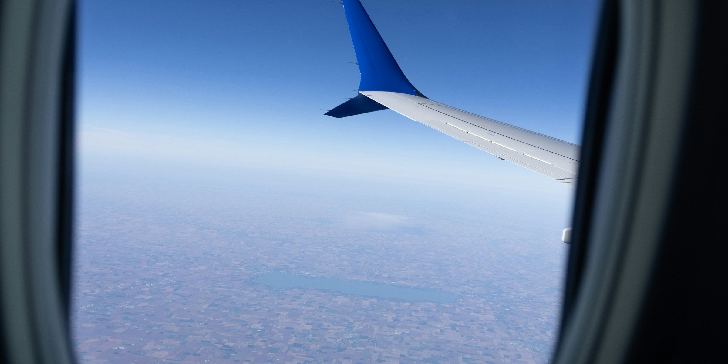 View of an aircraft wing and layered clouds through a cabin window in soft daylight