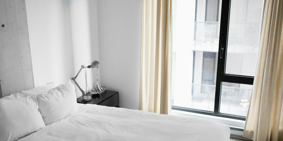 Made hotel bed with white linens beside a window in soft neutral light