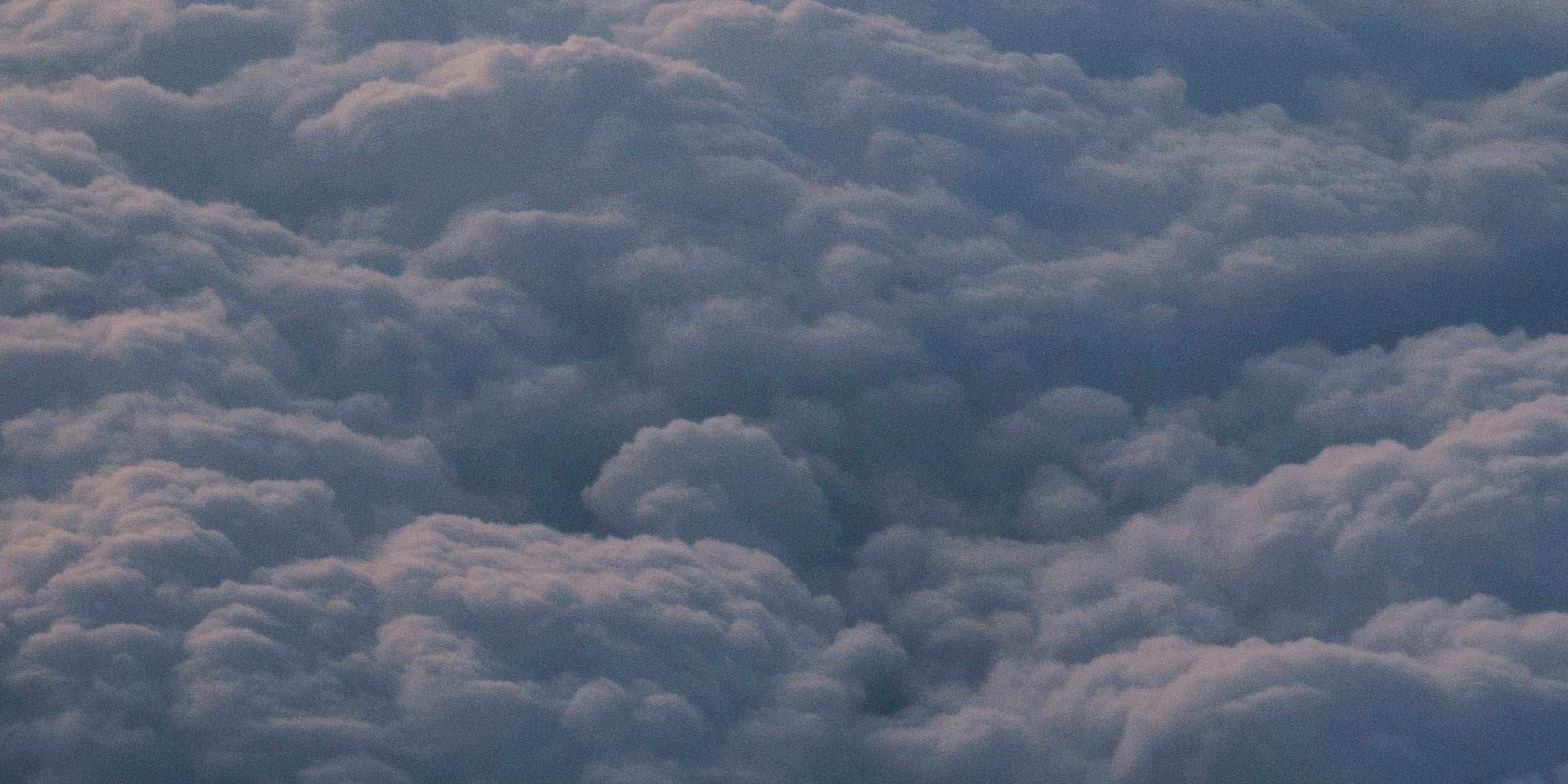 View through an airplane window showing clouds and sky at cruising altitude