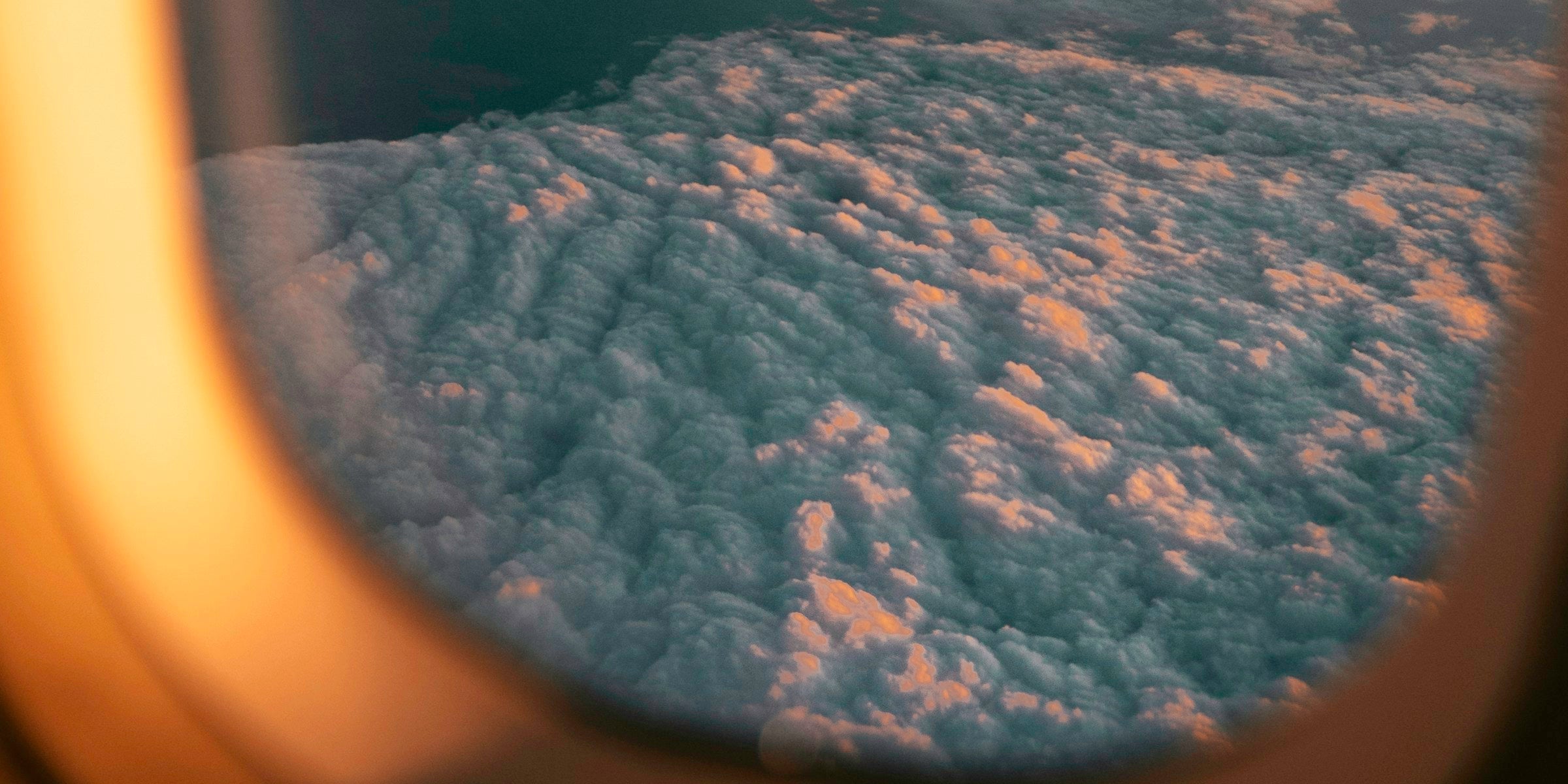 Layered clouds at sunset seen through an airplane window in soft, muted light
